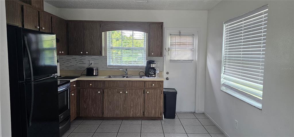 A kitchen features wood cabinets, a black refrigerator, a double sink, and tiled flooring — 12048 HENLEY AVENUE UNIT B, PORT CHARLOTTE, FL