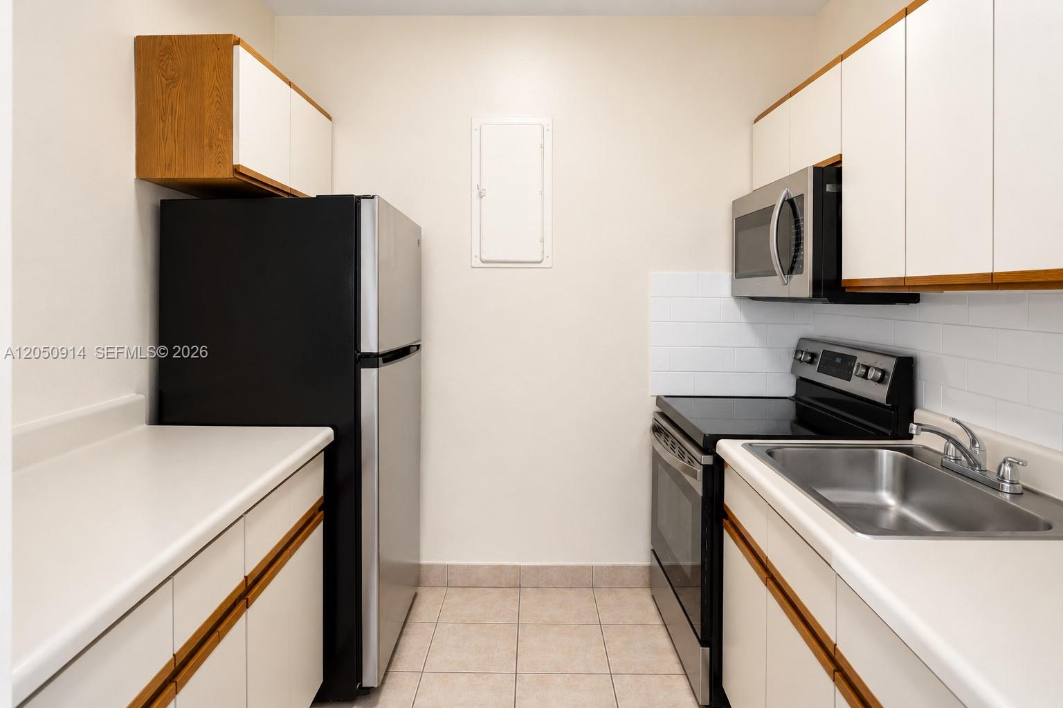 A galley kitchen features white cabinets, stainless steel appliances, and light-colored tile flooring — HOLLYWOOD, FL