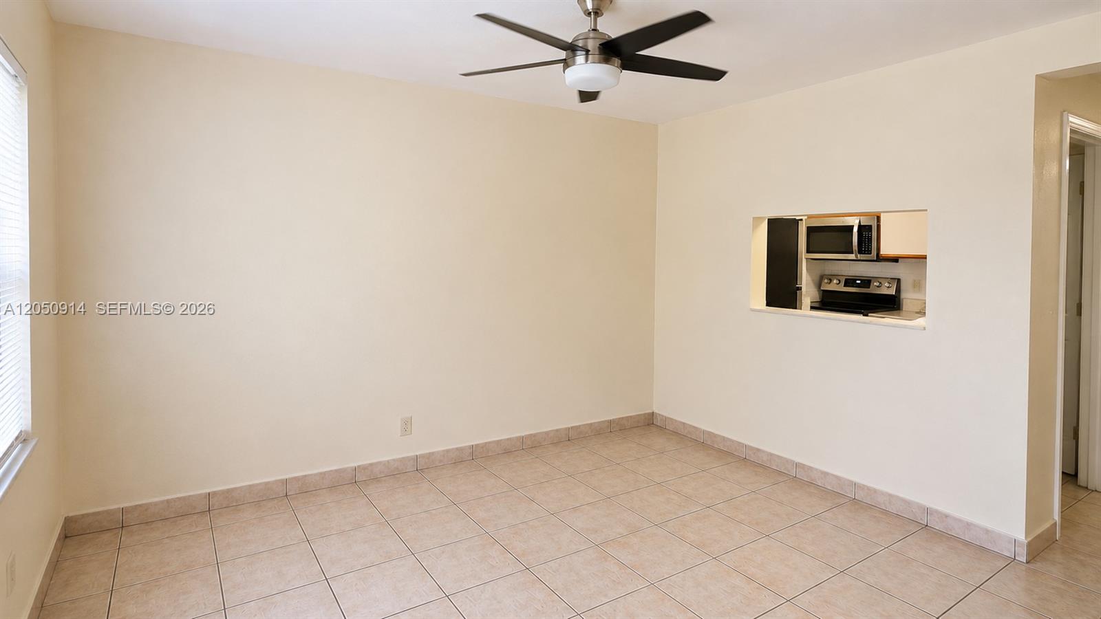 An empty room with beige walls, tile flooring, a ceiling fan, and a kitchen pass-through — HOLLYWOOD, FL
