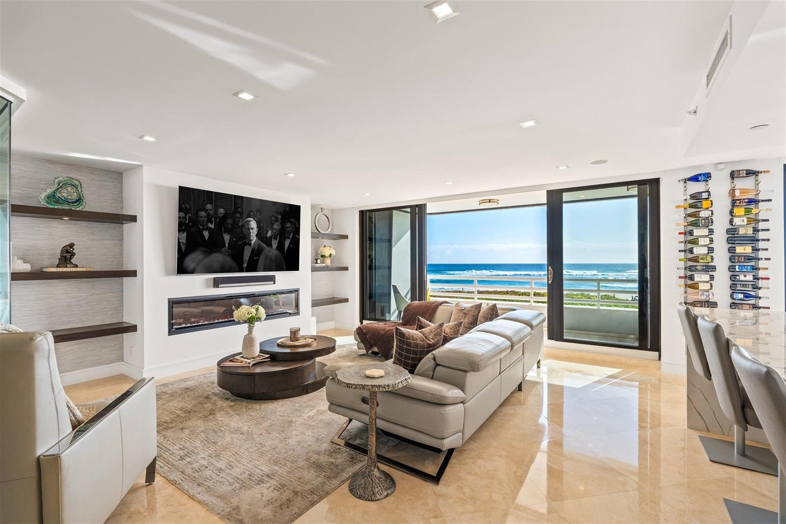 A modern living room features a fireplace, wall-mounted television, and sliding glass doors overlooking the ocean — 1400 S Ocean Boulevard # 103, Boca Raton FL 33432, BOCA RATON, FL