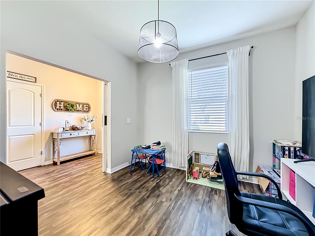 A room with wood-look flooring, a window with white curtains, and a child's play area — 11205 BRIGHTON KNOLL LOOP, RIVERVIEW, FL
