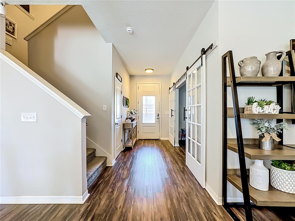 A bright entryway features wood-look flooring, a staircase, and sliding glass barn doors — 11205 BRIGHTON KNOLL LOOP, RIVERVIEW, FL