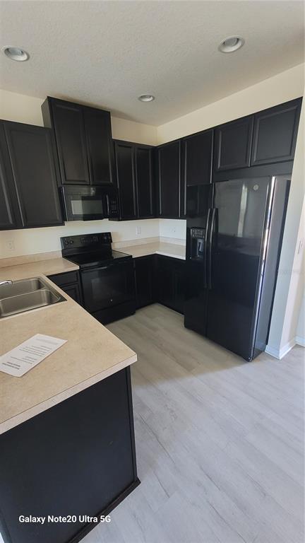 A kitchen features dark cabinets, light countertops, black appliances, and light-colored wood-look flooring — 7005 TOWERING SPRUCE DRIVE, RIVERVIEW, FL