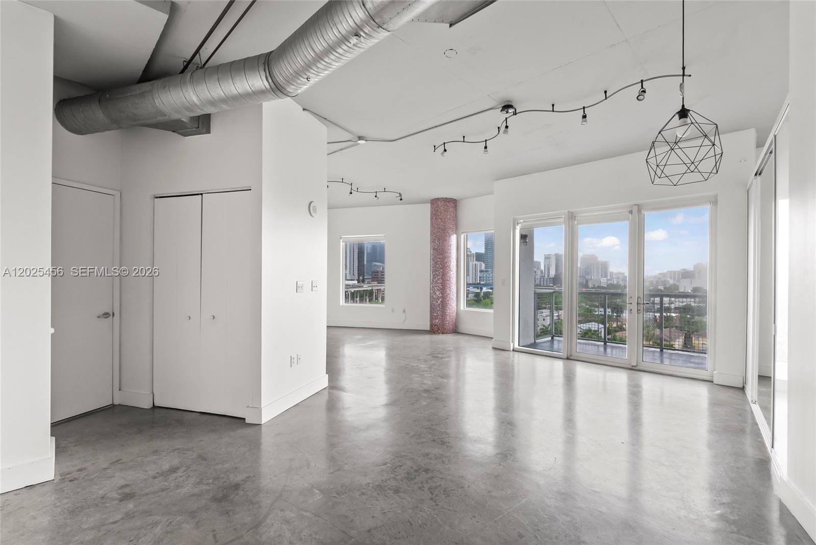An open-concept living area features concrete floors, exposed ductwork, and a balcony with city views — 10 SW South River Dr # 1006, Miami FL 33130, MIAMI, FL