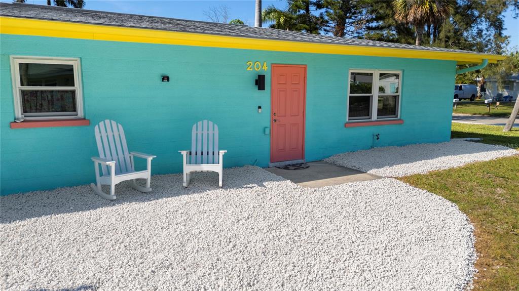 A turquoise house exterior features a coral door, two white rocking chairs, and gravel landscaping — 204 29TH STREET, HOLMES BEACH, FL