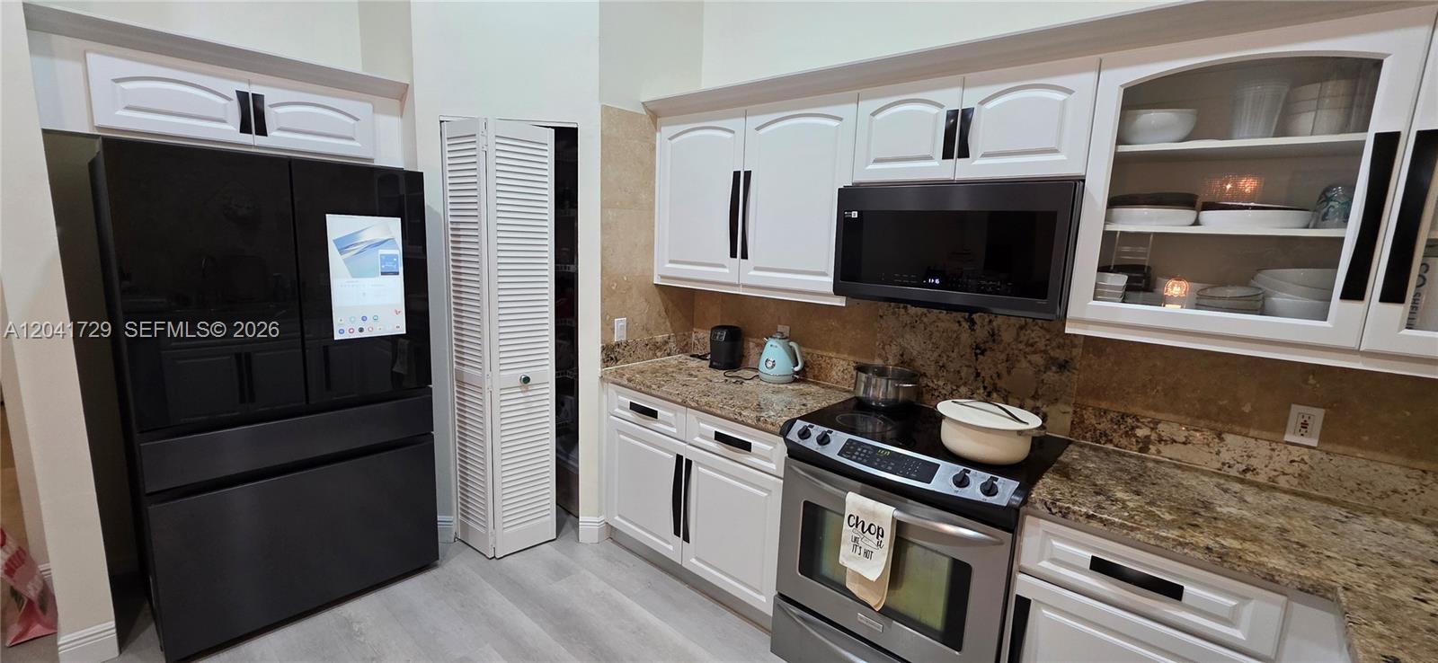 A kitchen features white cabinets, granite countertops, a black refrigerator, and a stainless steel stove — 5010 Perignon Way, Coral Springs FL 33067, CORAL SPRINGS, FL