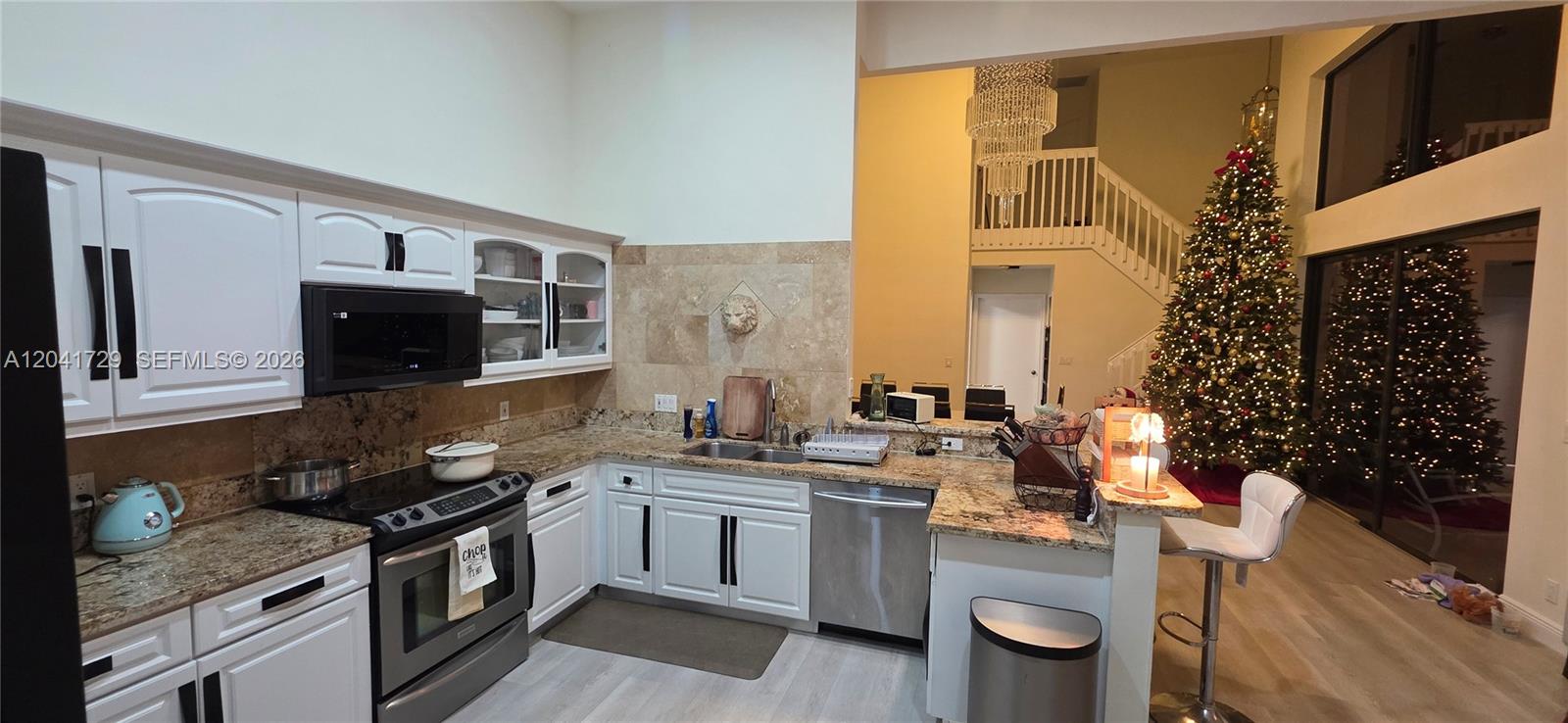A kitchen with white cabinets, granite countertops, and stainless steel appliances overlooks a living area — 5010 Perignon Way, Coral Springs FL 33067, CORAL SPRINGS, FL