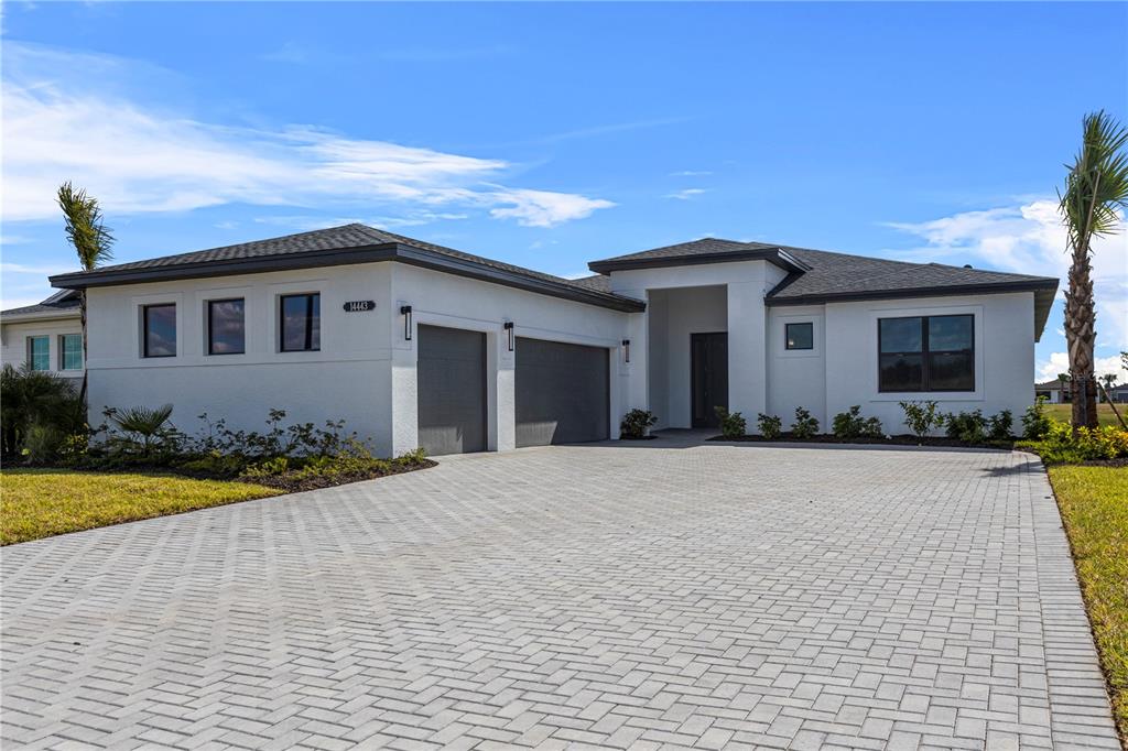 A modern single-story house with a white stucco exterior and a gray paver driveway — 14443 COASTAL WOODLAND LANE, PARRISH, FL