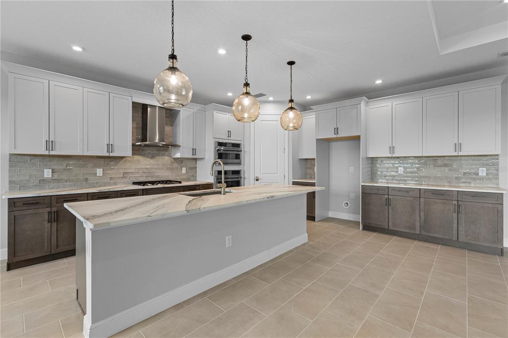 A kitchen features a large island, two-toned cabinetry, stainless steel appliances, and tile flooring — 14443 COASTAL WOODLAND LANE, PARRISH, FL