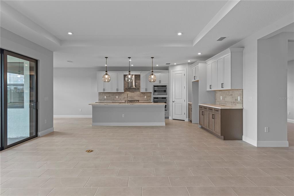 A modern kitchen features white cabinetry, a central island with pendant lights, and tile flooring — 14443 COASTAL WOODLAND LANE, PARRISH, FL
