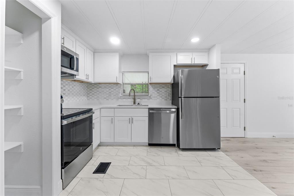 A kitchen with white cabinets, stainless steel appliances, and light-colored marble-look tile flooring — 130 FLORENCE BOULEVARD, DEBARY, FL