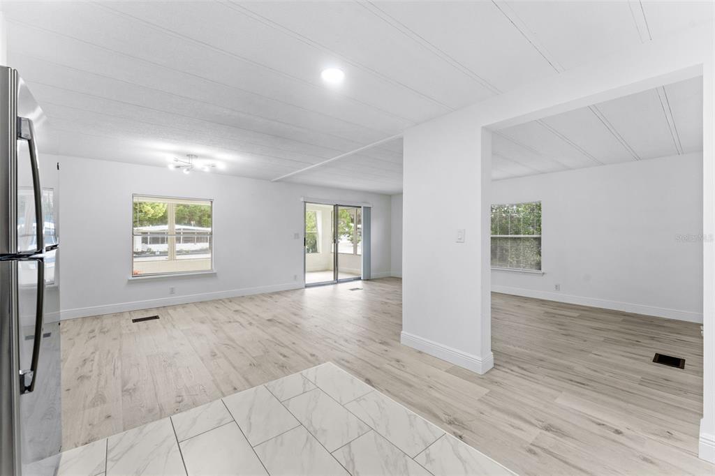 A bright, open-concept living area features light wood-look flooring, white walls, and sliding glass doors — 130 FLORENCE BOULEVARD, DEBARY, FL