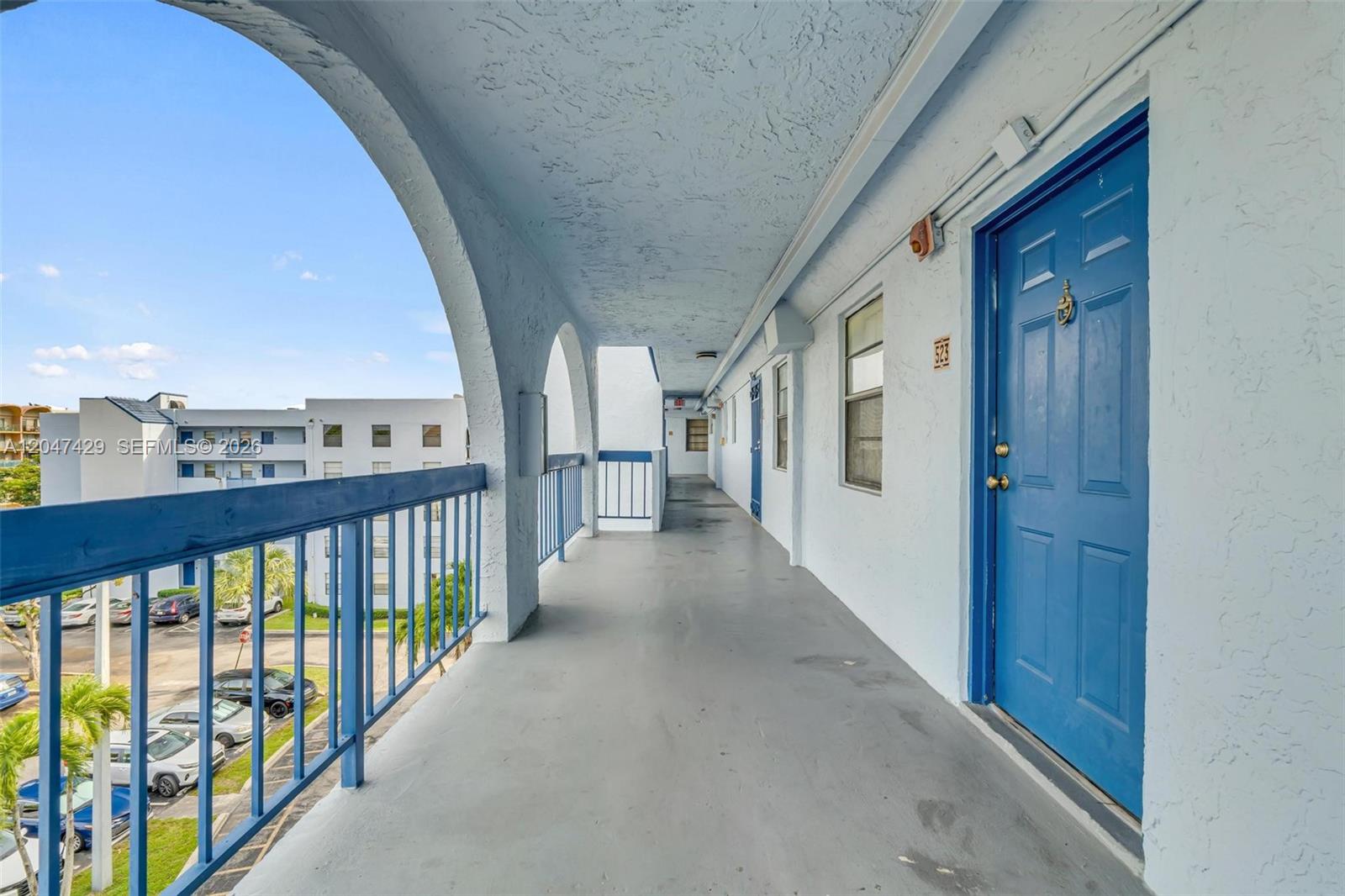 An outdoor apartment walkway features blue doors, arched openings, and a metal railing overlooking parking — 9460 Fontainebleau Blvd # 519, Miami FL 33172, MIAMI, FL