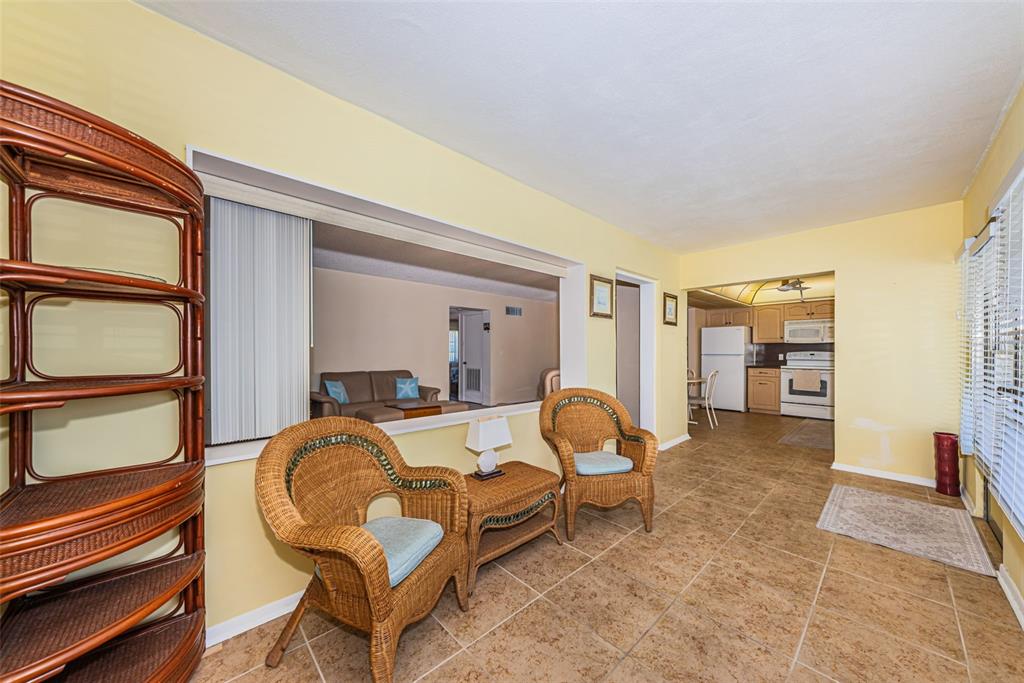 A sunroom with tile floors features two wicker chairs, a small table, and a pass-through window — 4700 COVE CIRCLE UNIT 208, ST PETERSBURG, FL