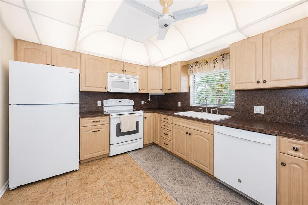 A kitchen with light wood cabinets, white appliances, dark countertops, and a vaulted ceiling — 4700 COVE CIRCLE UNIT 208, ST PETERSBURG, FL