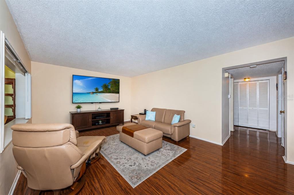 A living room with wood flooring, a leather sofa and recliner, and a wall-mounted television — 4700 COVE CIRCLE UNIT 208, ST PETERSBURG, FL