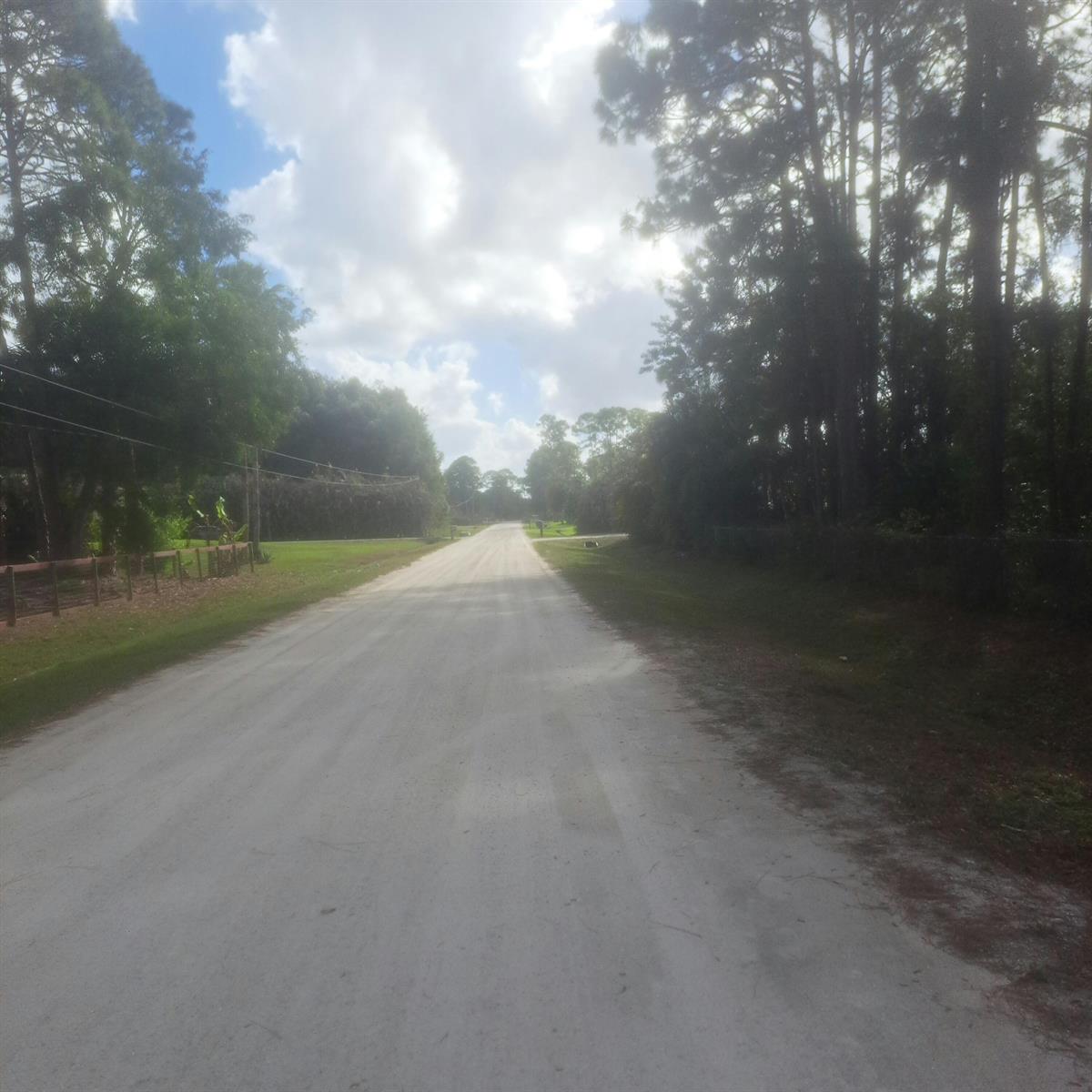 A dirt road stretches into the distance, flanked by trees and a wooden fence — 14845 62nd Court N, FL 33470, FL