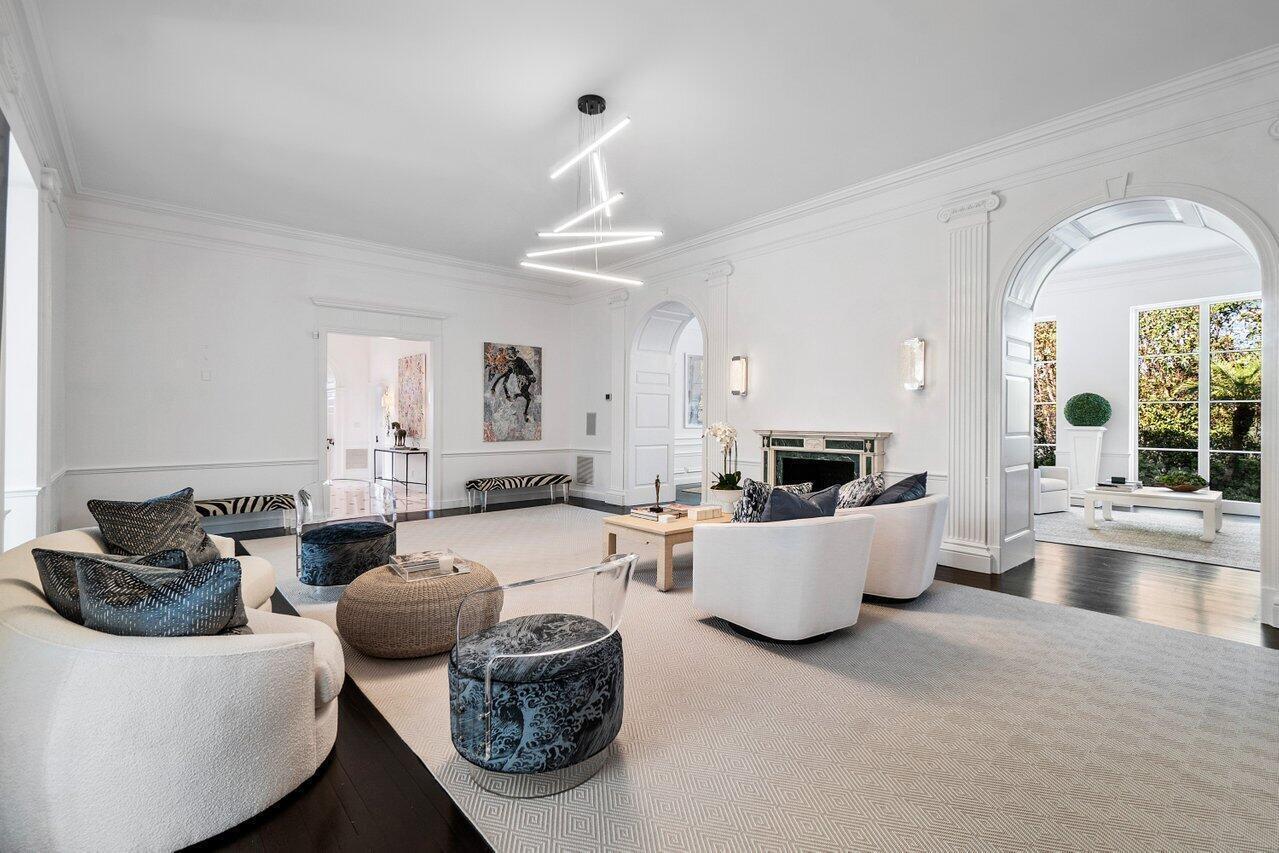 A bright, white living room features curved armchairs, a modern light fixture, and arched doorways — 100 Regents Park Road, Palm Beach FL 33480, PALM BEACH, FL