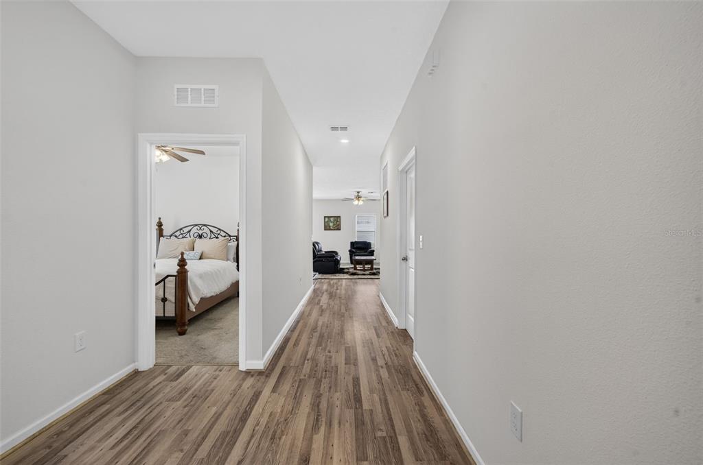 A hallway with wood-look flooring leads to a bedroom on the left and living area — 16434 BLOOMING CHERRY DRIVE, GROVELAND, FL
