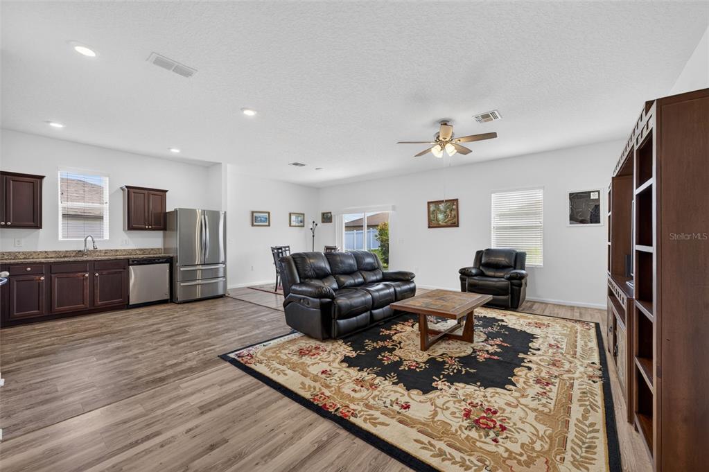 An open-concept living room and kitchen featuring dark wood cabinets, stainless appliances, and wood flooring — 16434 BLOOMING CHERRY DRIVE, GROVELAND, FL
