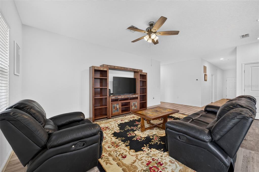 A living room features black leather furniture, a wooden entertainment center, and a patterned rug — 16434 BLOOMING CHERRY DRIVE, GROVELAND, FL