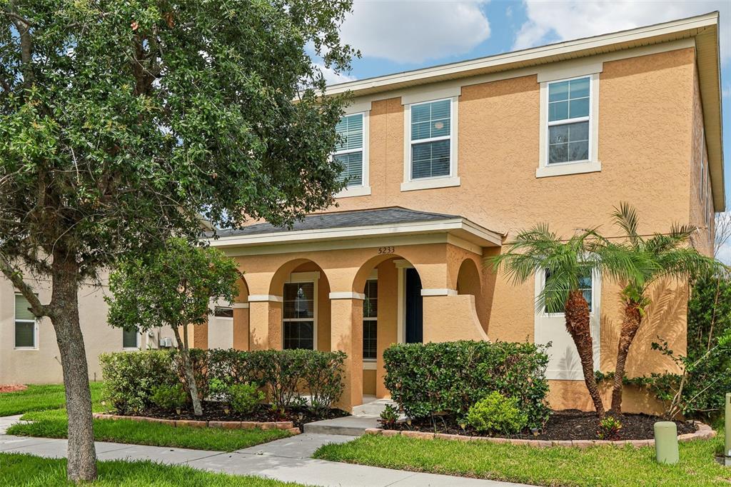 A two-story tan stucco house with an arched front porch and a landscaped front yard — 5233 SUNCATCHER DRIVE, WESLEY CHAPEL, FL