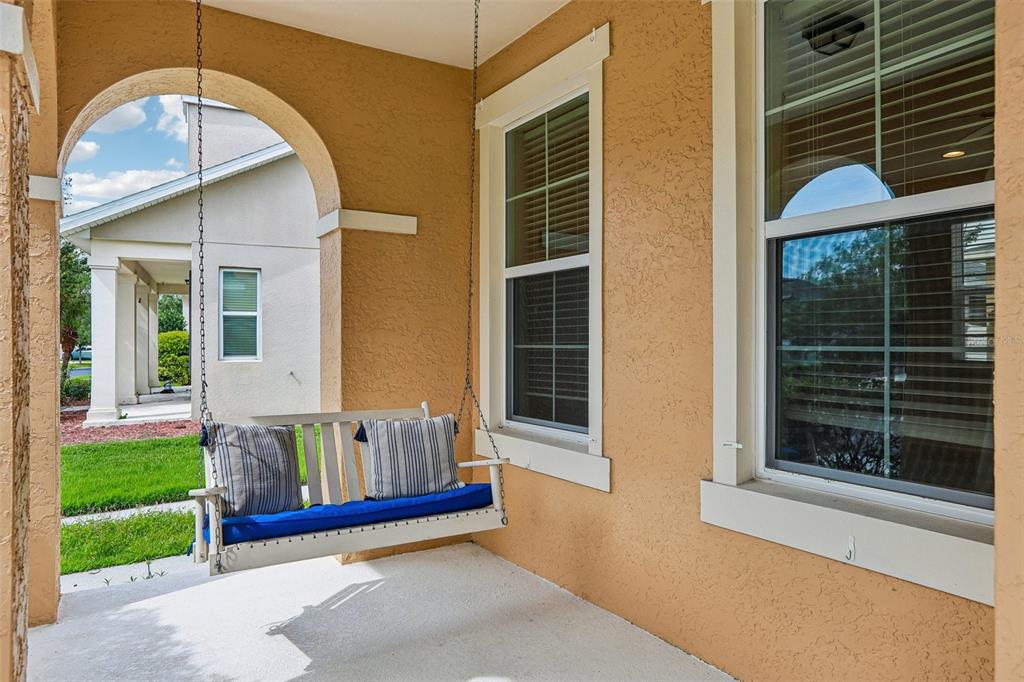 A covered porch features a white hanging bench with blue cushions and two windows — 5233 SUNCATCHER DRIVE, WESLEY CHAPEL, FL