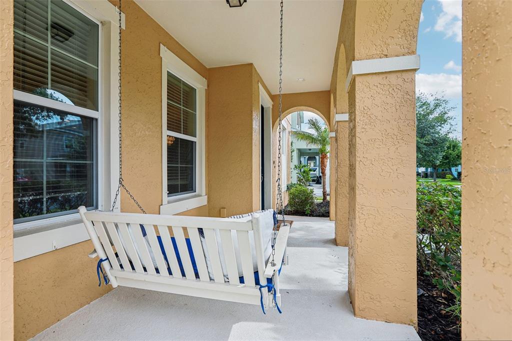 A covered porch features a white hanging bench, stucco columns, and an arched entryway — 5233 SUNCATCHER DRIVE, WESLEY CHAPEL, FL