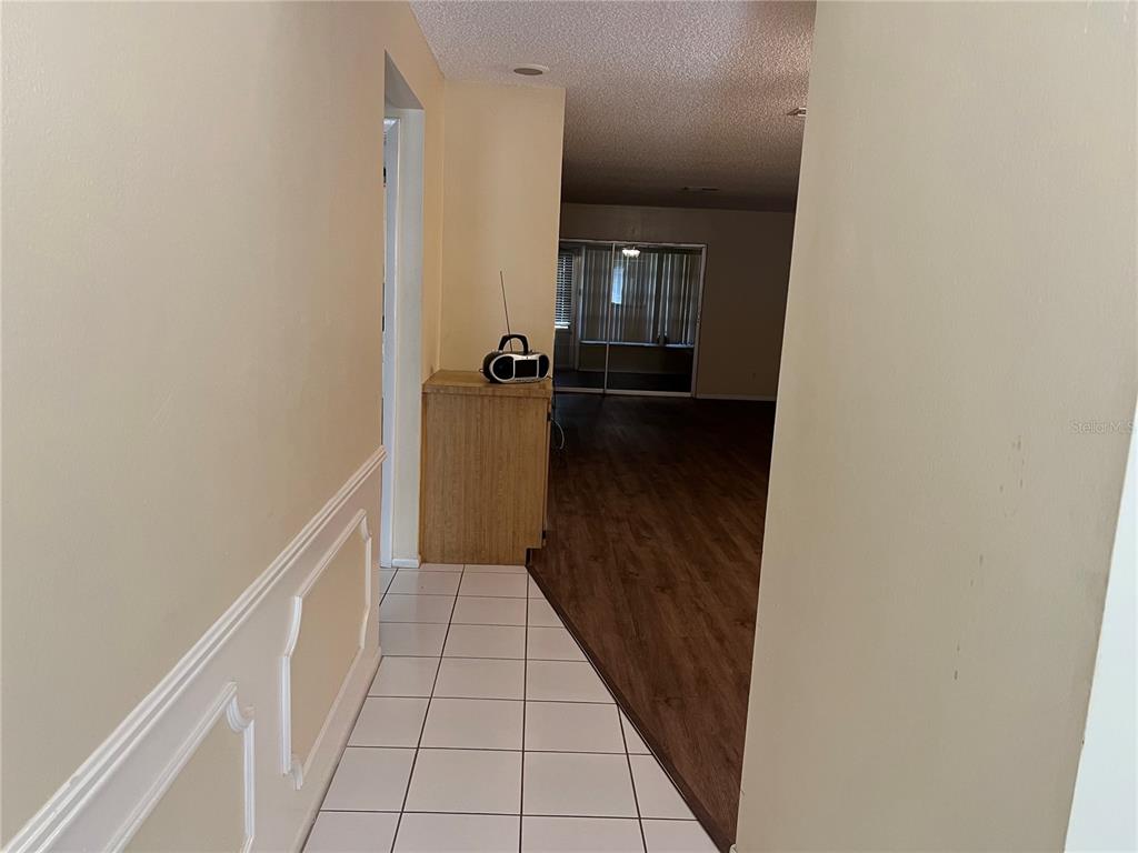 A hallway with white tile flooring transitions into a living area with wood-look flooring — 2225 LARK CIRCLE W UNIT E, PALM HARBOR, FL