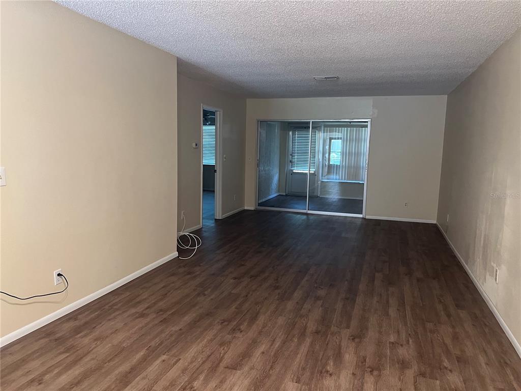 An empty living room features wood-look flooring, beige walls, and a sliding glass door — 2225 LARK CIRCLE W UNIT E, PALM HARBOR, FL