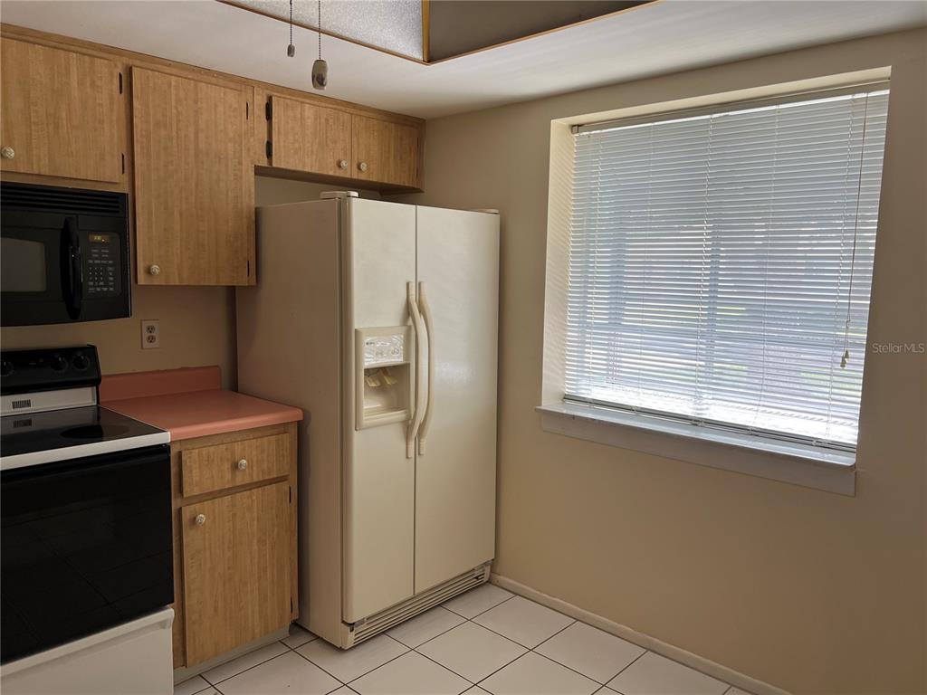 A kitchen features light wood cabinets, a pink countertop, a white refrigerator, and tiled flooring — 2225 LARK CIRCLE W UNIT E, PALM HARBOR, FL