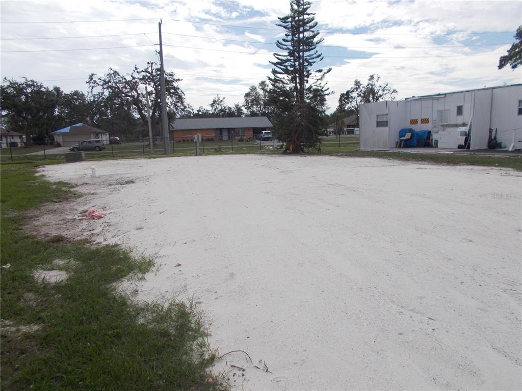 A large, cleared sandy lot sits in front of a white building and a tall tree — 5094 PALENA BOULEVARD, NORTH PORT, FL