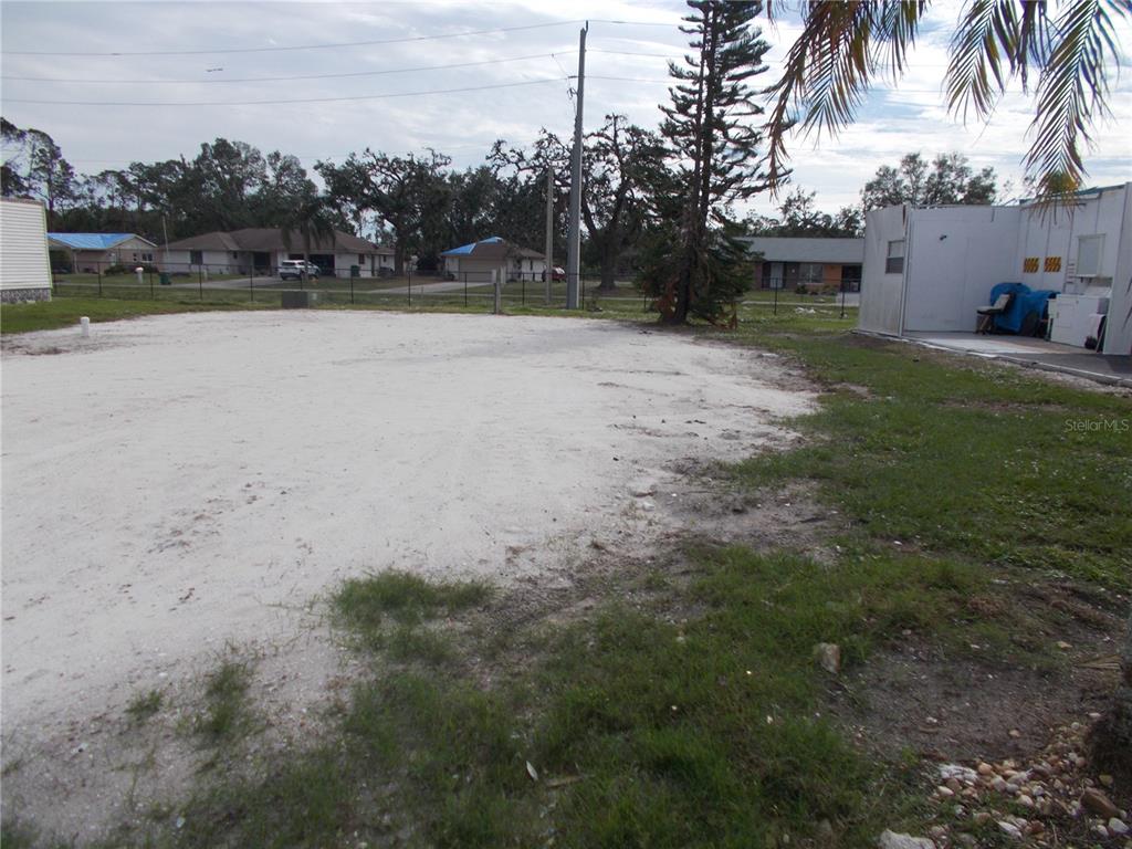 A large, sandy vacant lot sits next to a white structure under a cloudy sky — 5094 PALENA BOULEVARD, NORTH PORT, FL