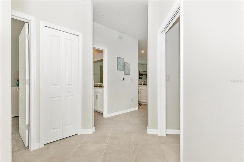 A hallway with light-colored tile flooring leads to a bathroom and an open kitchen area — 12280 WELLEN GOLF STREET UNIT 301, VENICE, FL