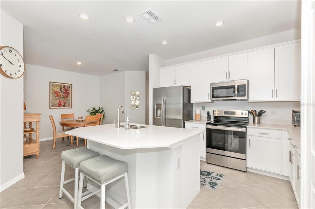 A modern kitchen features white cabinetry, stainless steel appliances, a central island, and adjacent dining area — 12280 WELLEN GOLF STREET UNIT 301, VENICE, FL