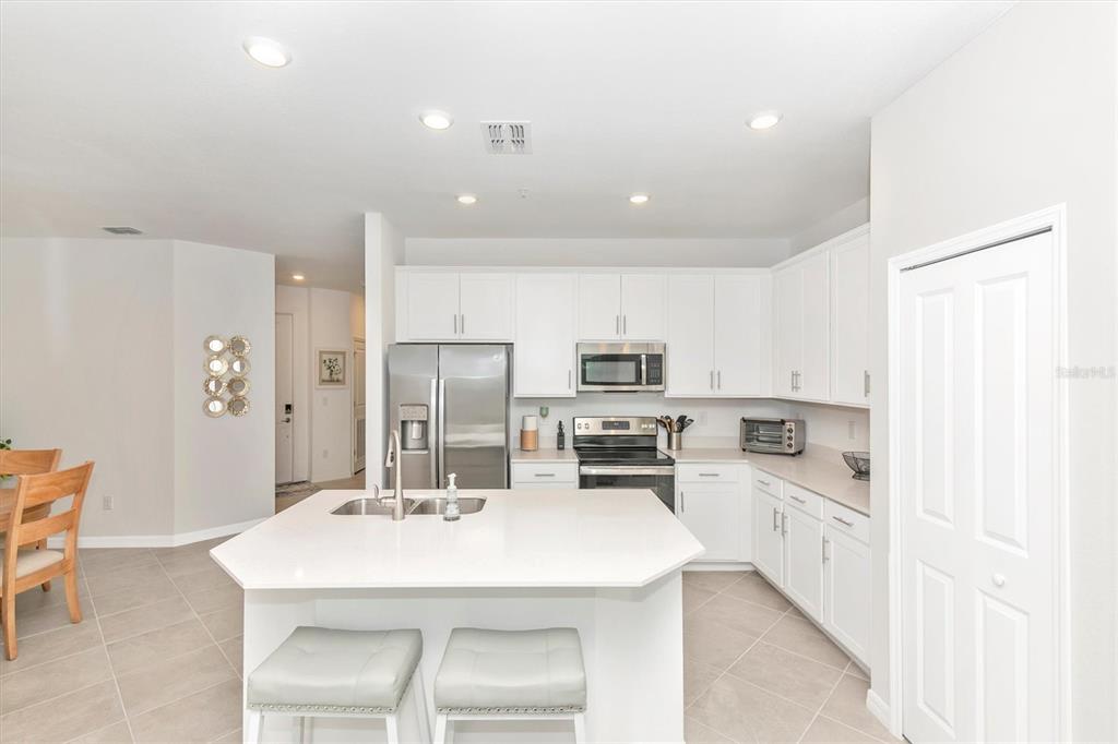 A modern kitchen features white cabinetry, stainless steel appliances, a central island, and tile flooring — 12280 WELLEN GOLF STREET UNIT 301, VENICE, FL