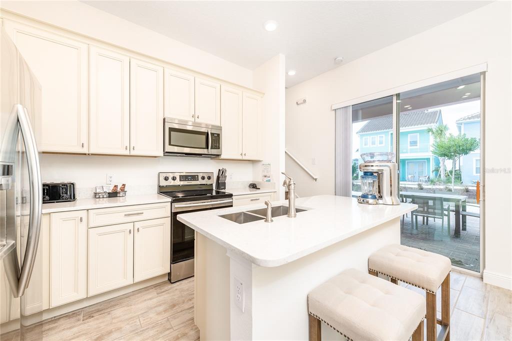 A modern kitchen features white cabinets, stainless steel appliances, a center island, and sliding glass doors — 8075 KNEE DEEP ROAD, KISSIMMEE, FL