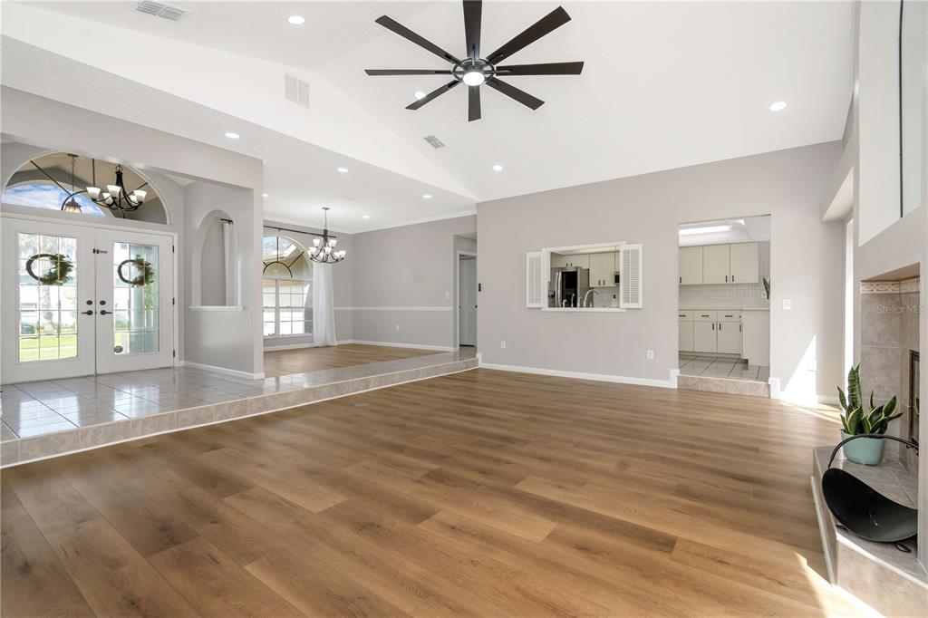A spacious living room with vaulted ceilings, wood-look flooring, and an adjacent tiled dining area — 13640 MORNING COURT, HUDSON, FL