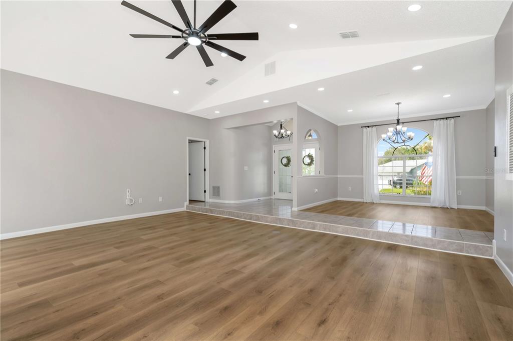 A living room with light gray walls, wood-look flooring, a vaulted ceiling, and a step-up area — 13640 MORNING COURT, HUDSON, FL