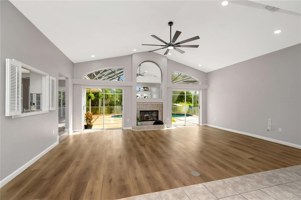 A spacious living room features light wood flooring, a fireplace, and sliding glass doors — 13640 MORNING COURT, HUDSON, FL