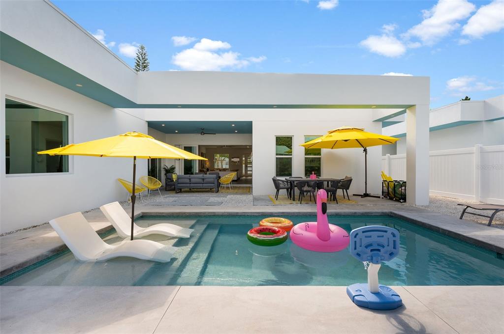 A modern backyard features a swimming pool with lounge chairs, umbrellas, and outdoor dining furniture — 2375 WALDEMERE STREET, SARASOTA, FL