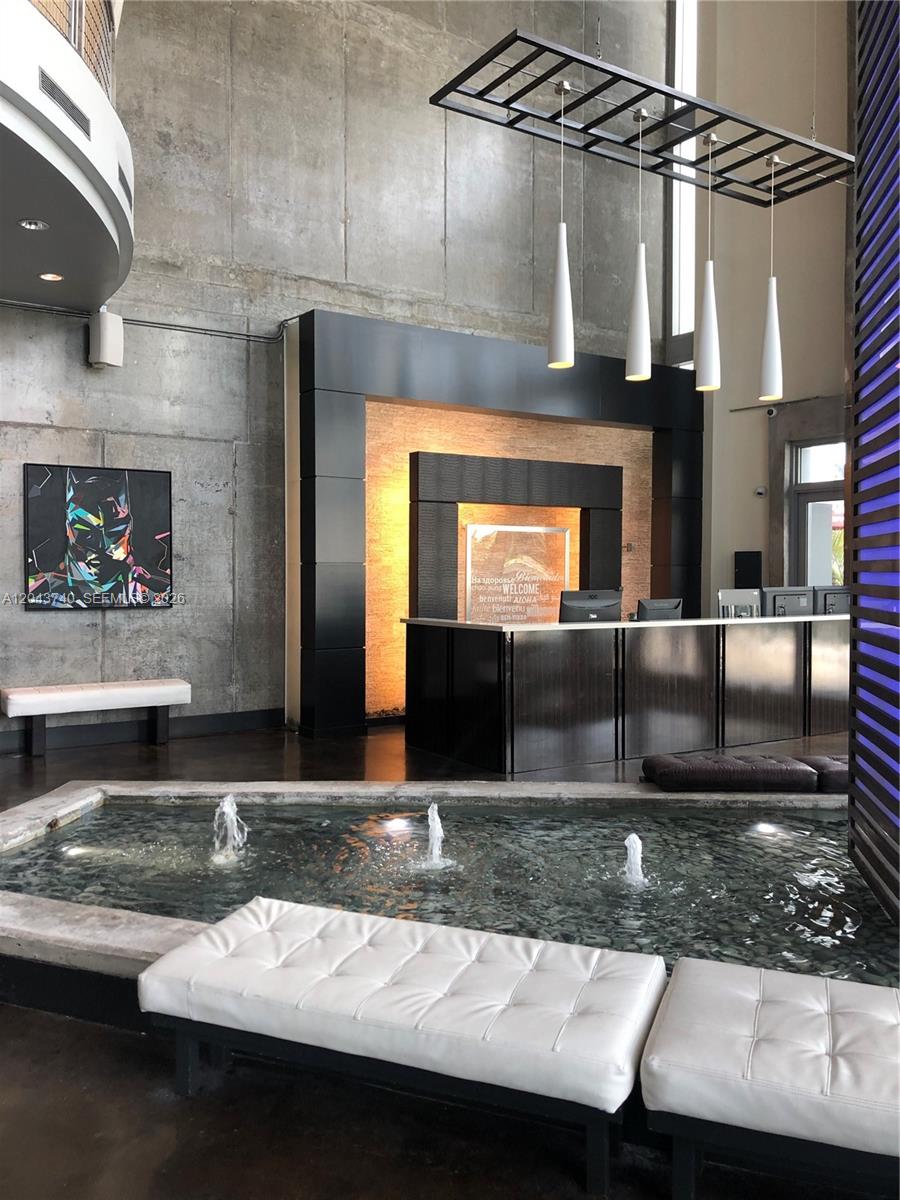 A modern lobby features a reception desk, a small indoor fountain, and concrete walls — 690 SW 1st Ct # 1019, Miami FL 33130, MIAMI, FL
