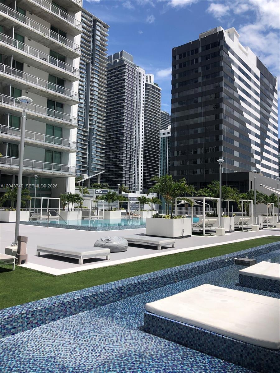 An outdoor pool deck features lounge chairs, planters, and modern high-rise buildings in the background — 690 SW 1st Ct # 1019, Miami FL 33130, MIAMI, FL