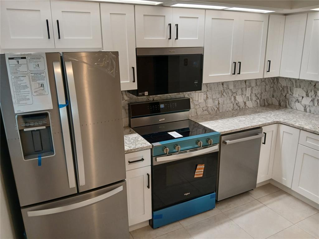 A kitchen features white cabinets, stainless steel appliances, and a marble-patterned backsplash and countertop — 1245 S MARTIN LUTHER KING JR AVENUE UNIT 104, CLEARWATER, FL