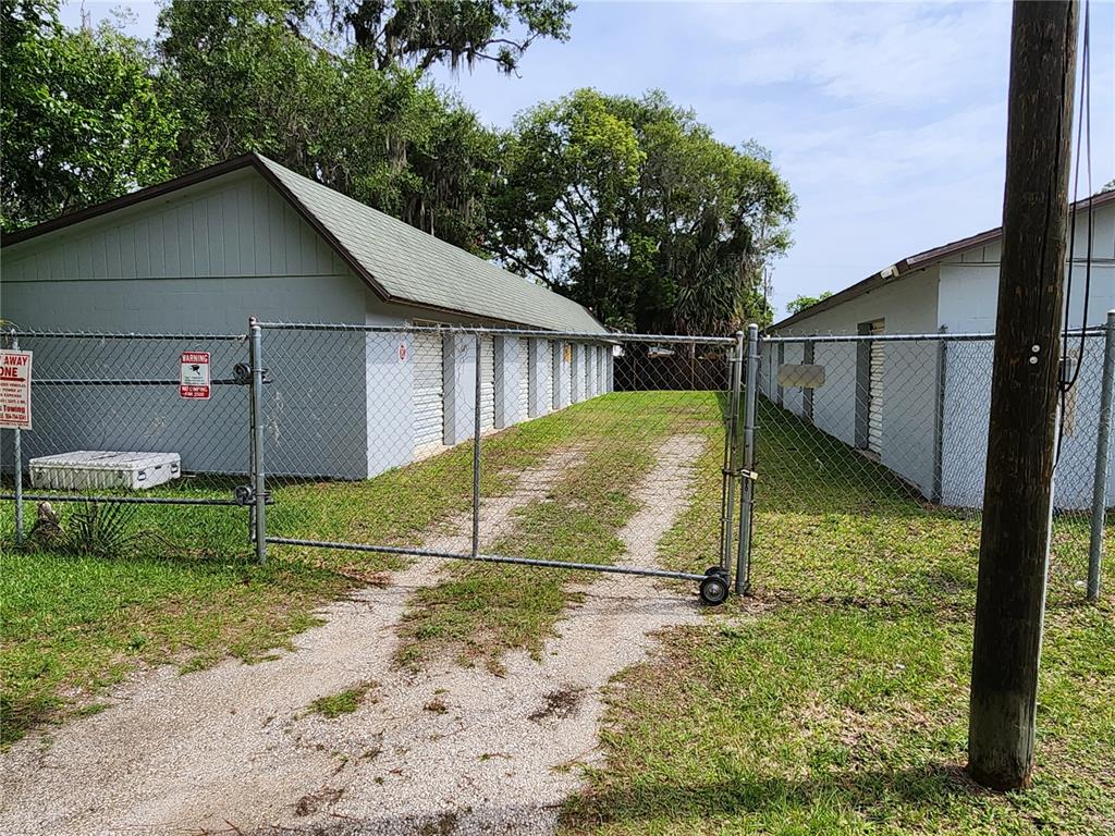 A fenced gravel driveway leads between two rows of storage units under a blue sky — 500 E COURT STREET, BUNNELL, FL