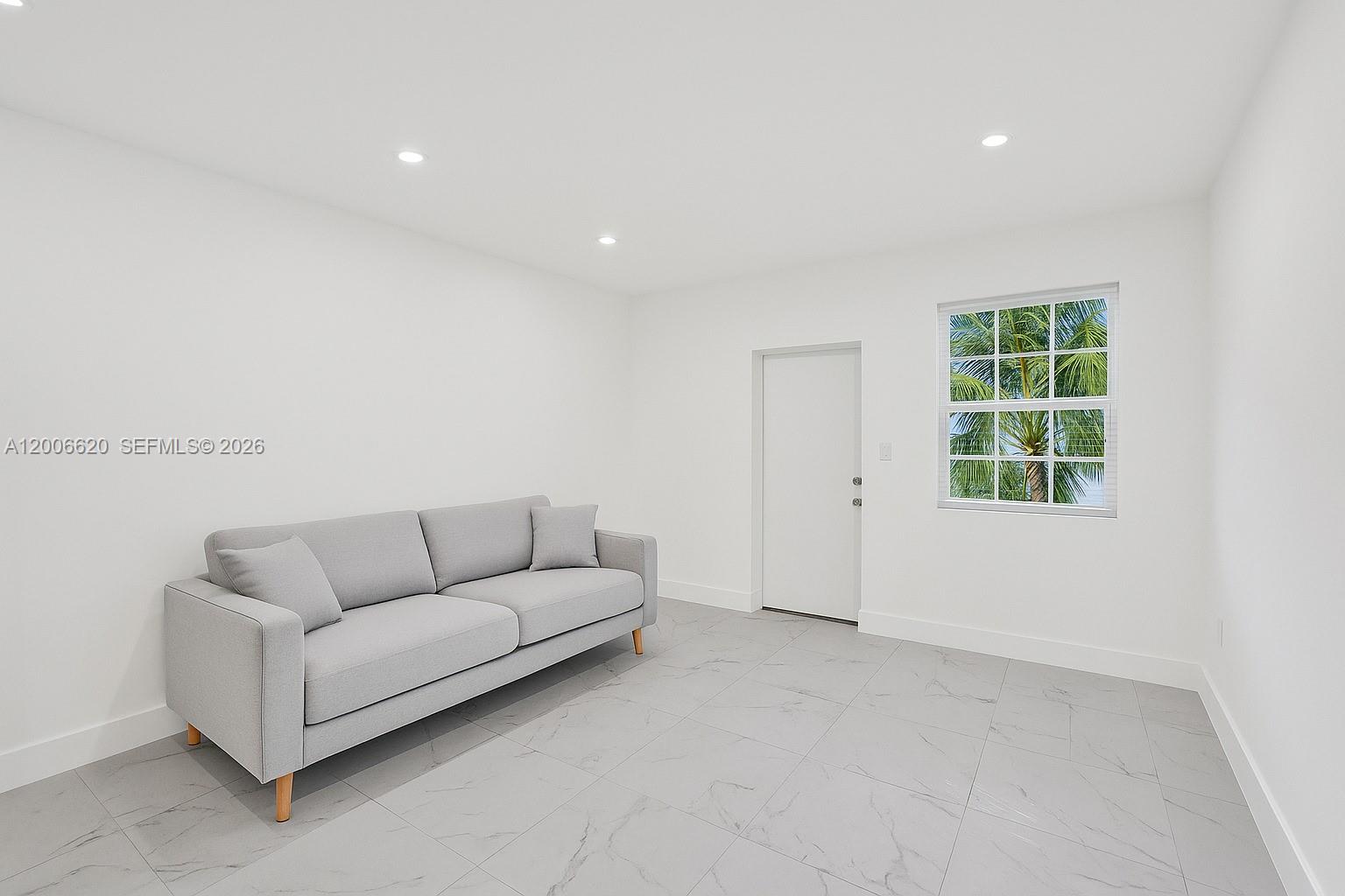 A minimalist room features a gray sofa, white walls, and light gray tiled flooring — 5807 SW 25th St # 0, West Park FL 33023, WEST PARK, FL