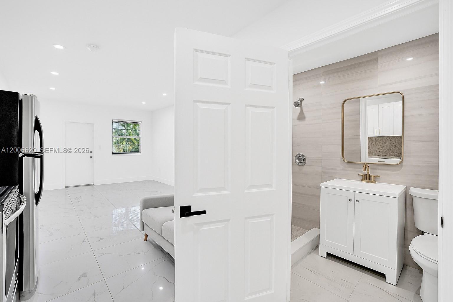 A white door opens to a bathroom with a vanity, toilet, and shower area — 5807 SW 25th St # 0, West Park FL 33023, WEST PARK, FL