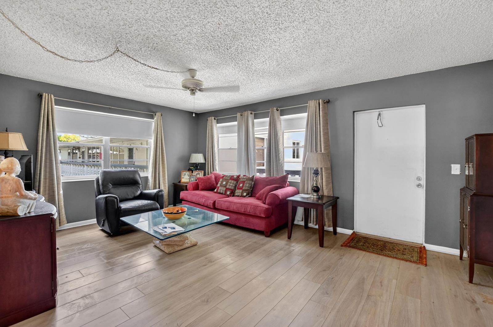 A living room features gray walls, wood-look flooring, a red sofa, and a glass coffee table — 313 Durham Circle # I, Deerfield Beach FL 33442, DEERFIELD BEACH, FL