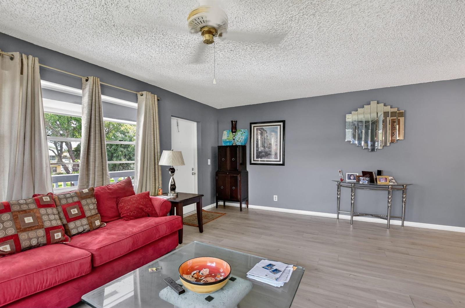 A living room features gray walls, wood-look flooring, a red sofa, and a ceiling fan — 313 Durham Circle # I, Deerfield Beach FL 33442, DEERFIELD BEACH, FL