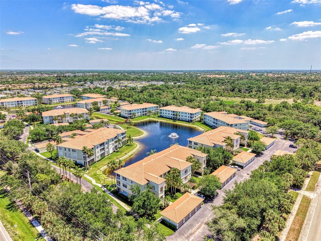 An aerial view shows multiple apartment buildings surrounding a central pond with a fountain — 900 SAN LINO CIRCLE UNIT # 910, VENICE, FL